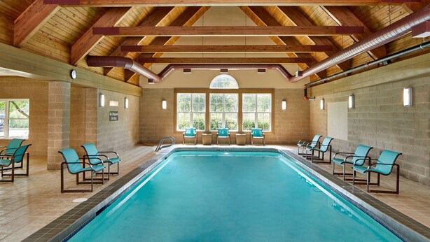 An indoor swimming pool with wooden beams, clear glass windows, and lounge chairs. - Residence Inn by Marriott Rochester West/Greece (Rochester)