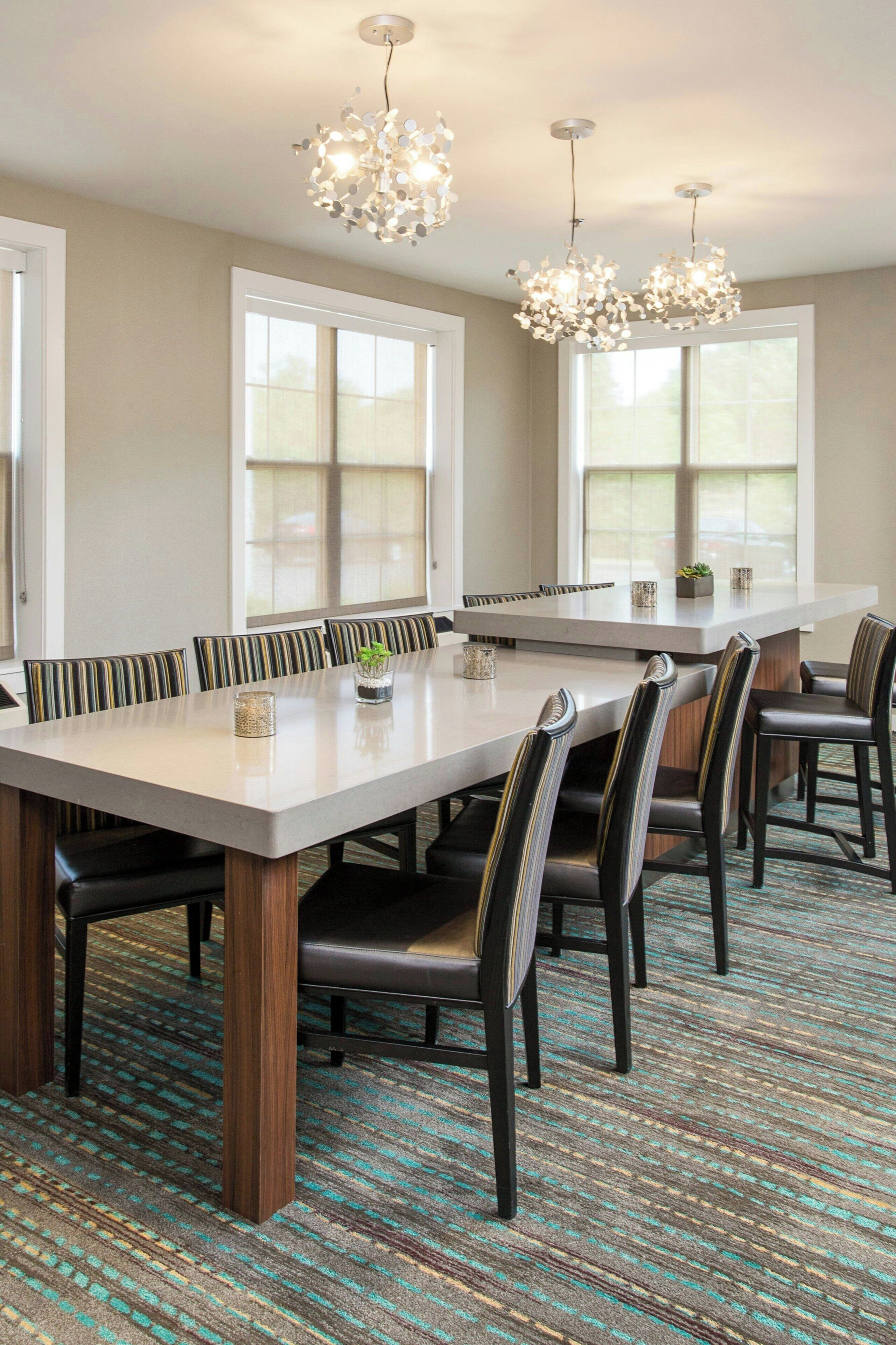 A dining area with a long table, multiple chairs, and pendant lighting.