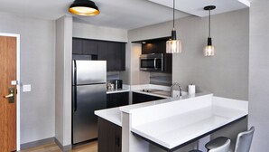 A modern kitchen with a stainless steel refrigerator, a microwave, and a sink with a white countertop. There are two pendant lights hanging above the sink. - Residence Inn by Marriott Rochester West/Greece (Rochester)