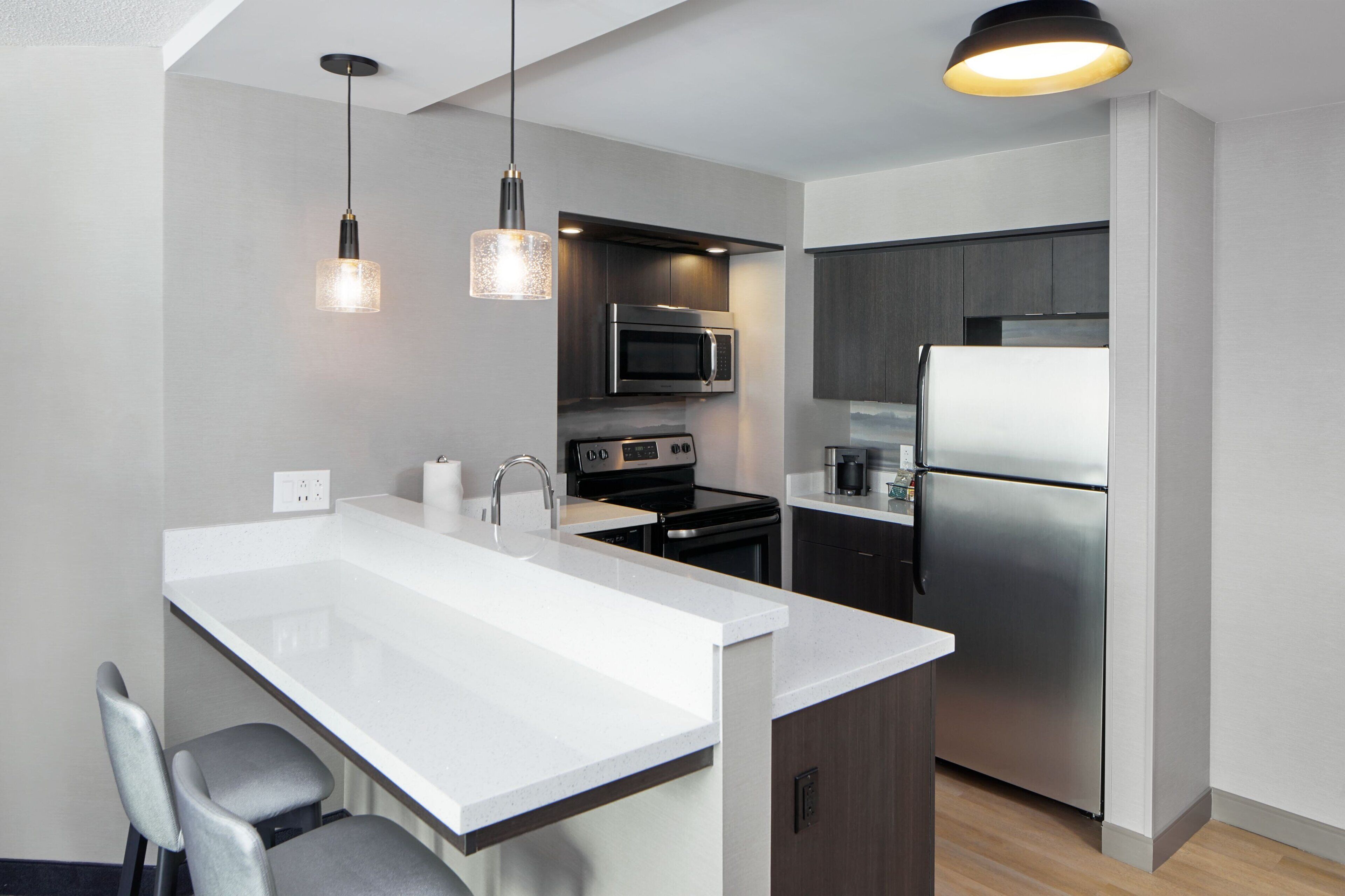 Une cuisine moderne avec un îlot central blanc, des appareils électroménagers en acier inoxydable et des luminaires suspendus.