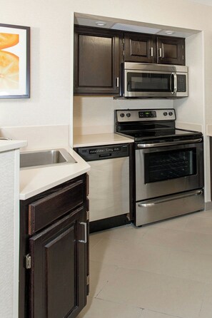 A compact kitchen with dark wooden cabinets, a stainless steel microwave, a built-in oven, and a dishwasher.