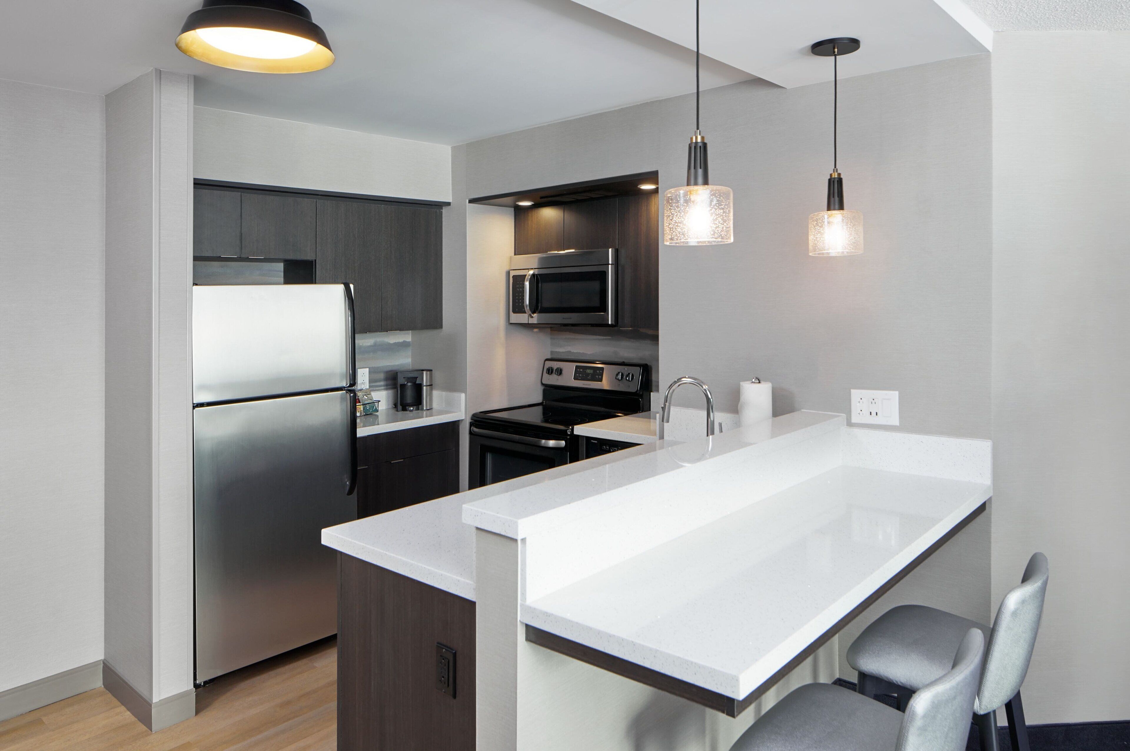 A modern kitchen with stainless steel appliances, a white countertop island, and pendant lighting.