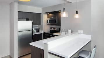 A modern kitchen with stainless steel appliances, a white countertop island, and pendant lighting.