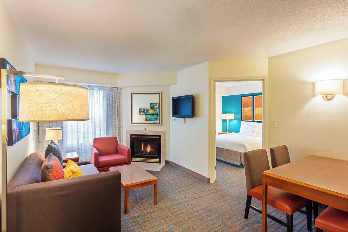 A hotel room with a sofa, armchair, dining table, and a fireplace.