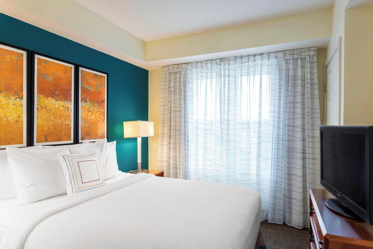 A hotel room with a large bed, a television, a nightstand, and a window with curtains.