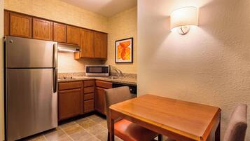 A compact kitchen with wooden cabinets, stainless steel appliances, a microwave, and a dining area with a table and chairs.