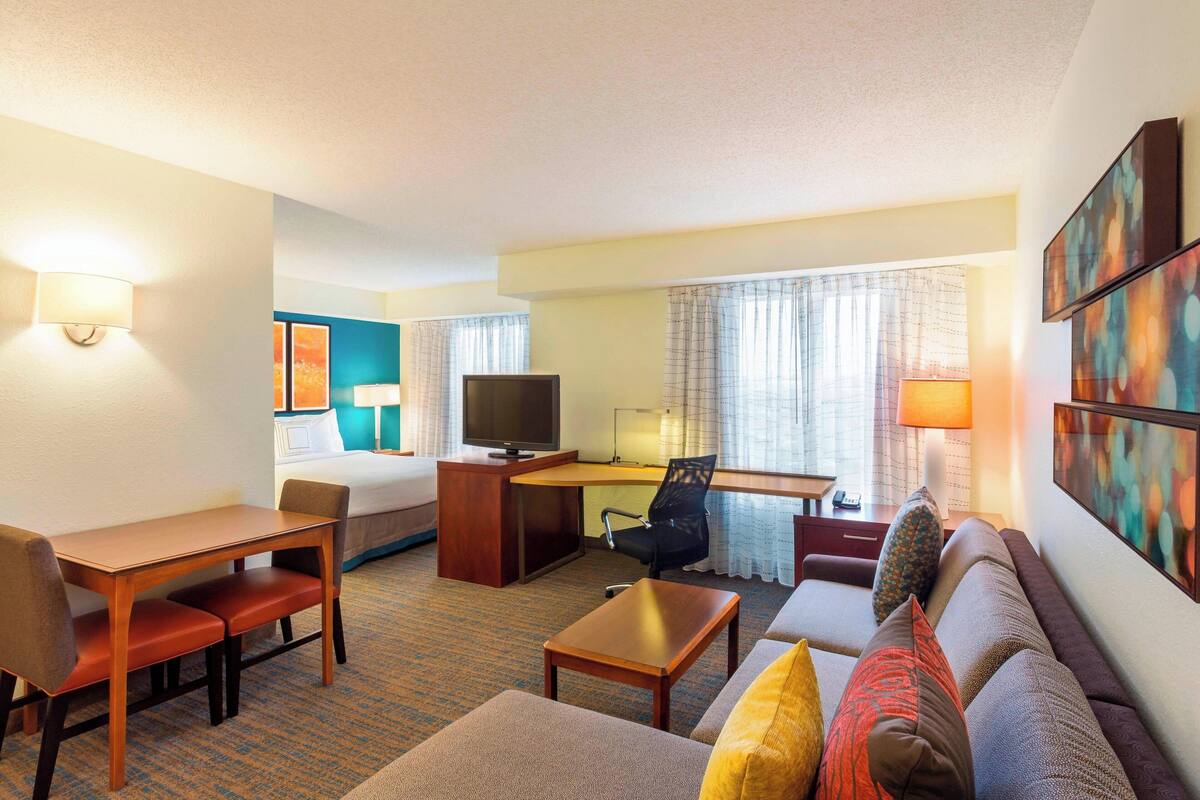 A hotel room with a bed, a desk with a computer, a television, a sofa, and a coffee table.
