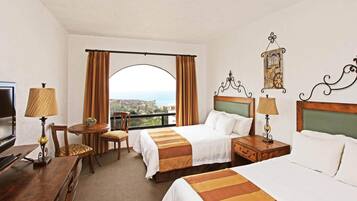 A hotel room with two beds, a TV, a dining table, and a view of the sea.
