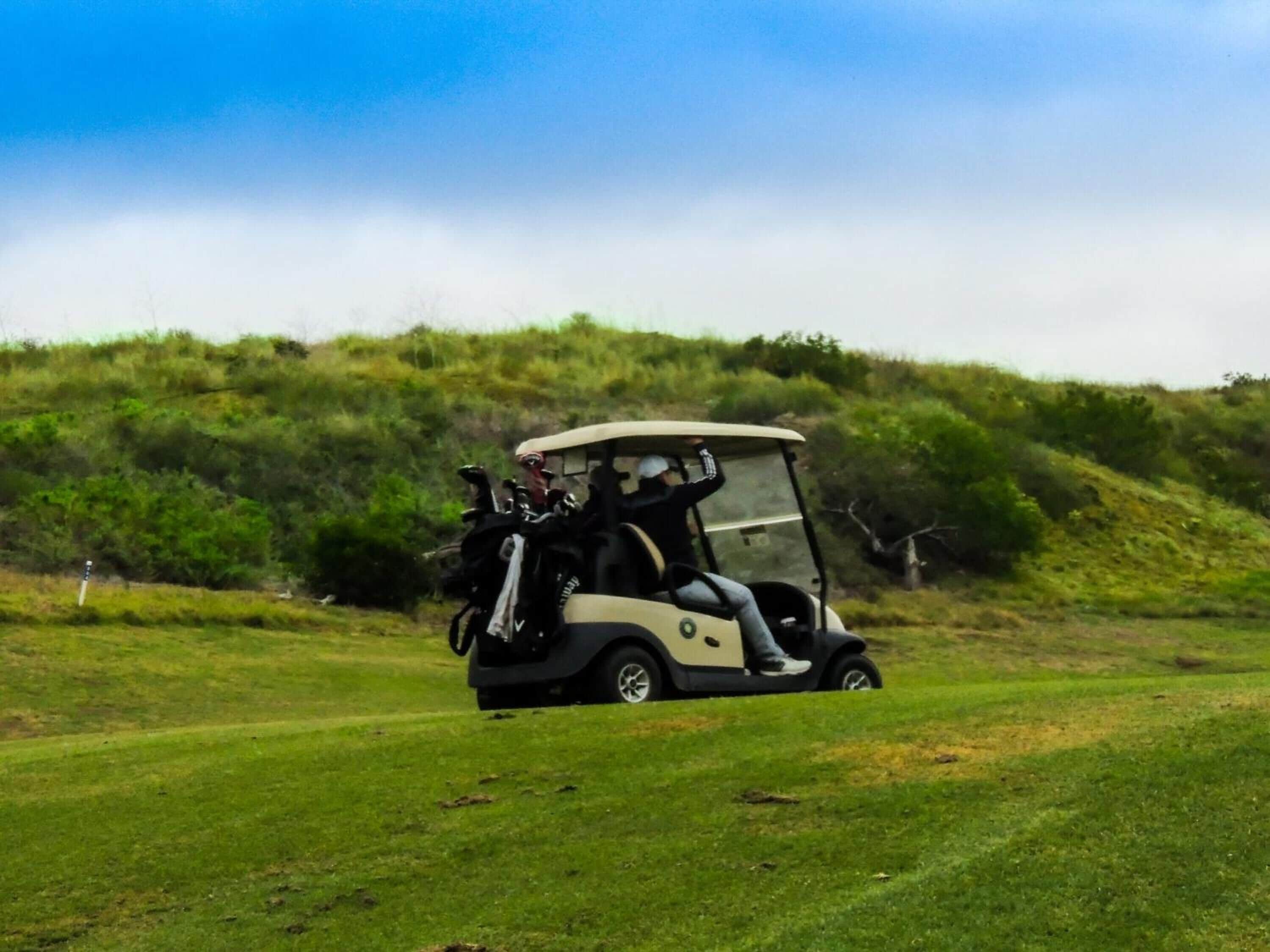 A golf cart on a grassy field with a hilly background.