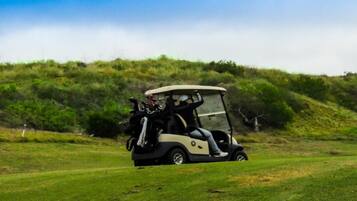 A golf cart on a grassy field with a hilly background.