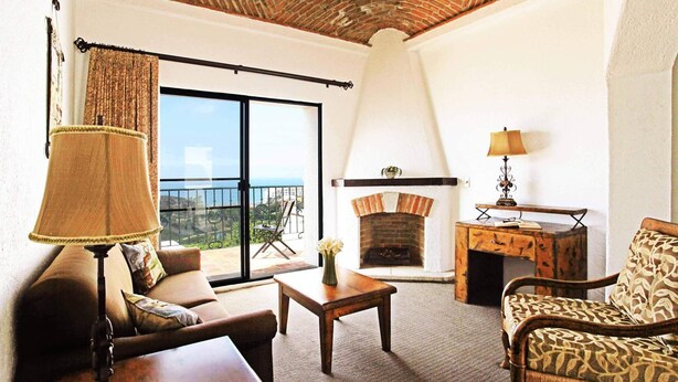 A cozy living room with a fireplace, a sofa, a table, and a view of the outdoors. - Real del Mar Hotel & Golf Resort (Tijuana)