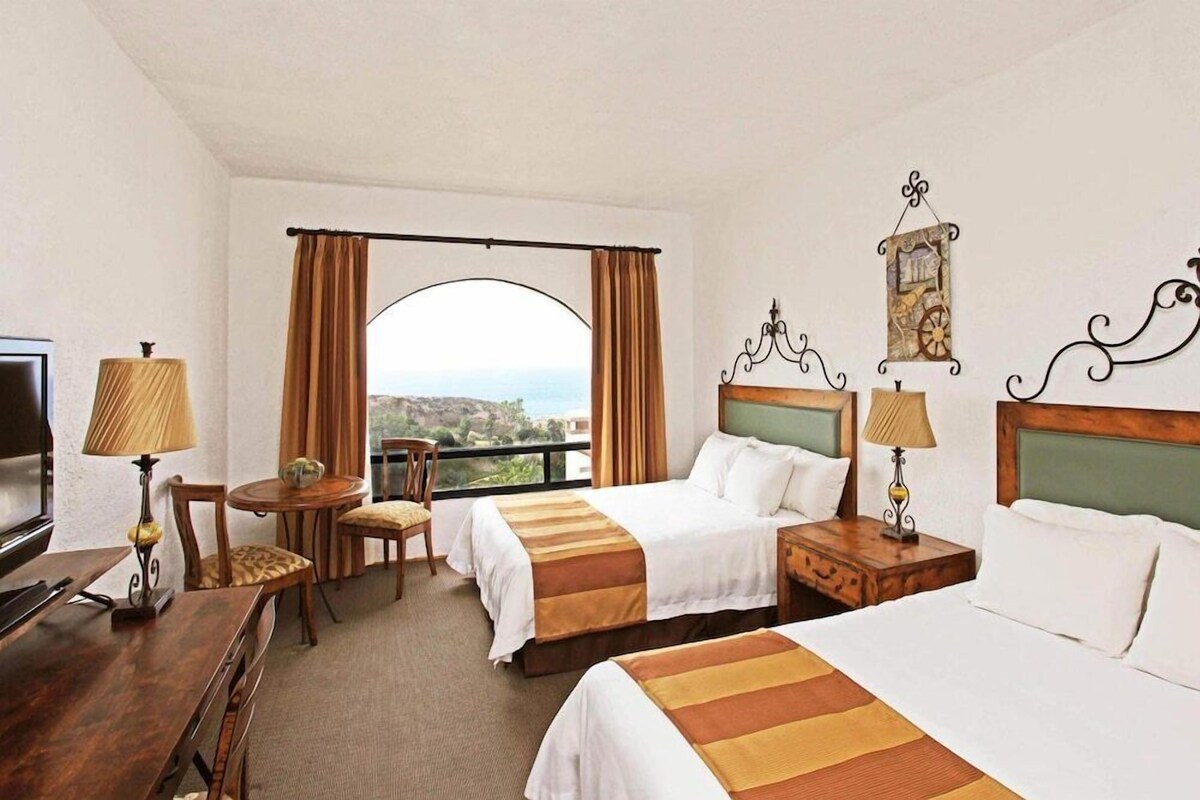 Une chambre d’hôtel avec deux lits, une télévision, un bureau et vue sur la mer.