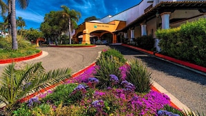 A hotel entrance with a curved driveway, palm trees, and colorful flower beds. - Real del Mar Hotel & Golf Resort (Tijuana)