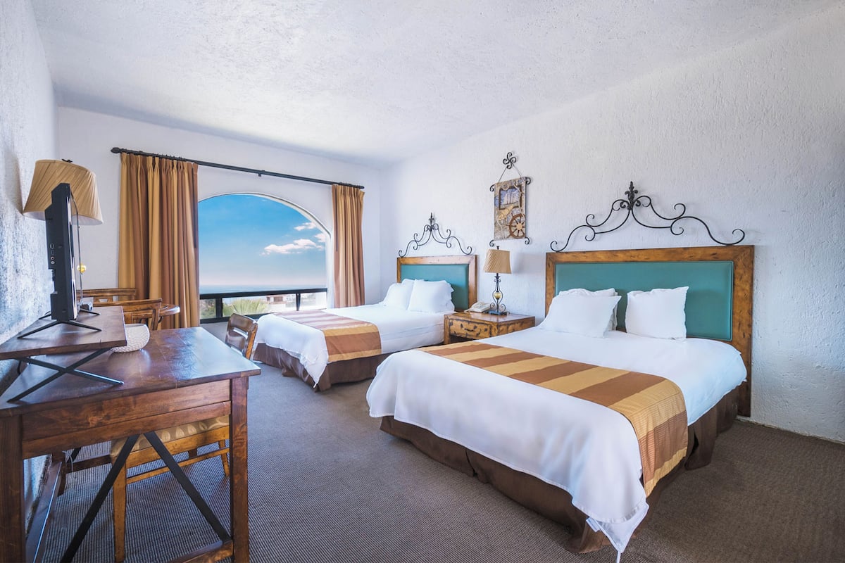 A hotel room with two beds, a desk, and a view of the sky.
