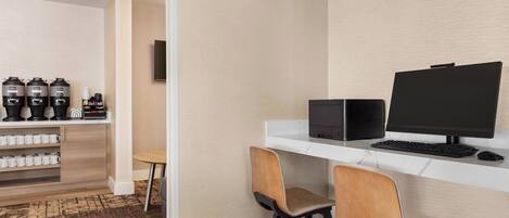 A modern workspace with a computer, two chairs, and a coffee station with multiple coffee makers and cups.