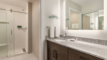 Un baño moderno con cabina de ducha de vidrio, un espejo grande y encimera de granito con lavabo.