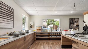 Une cuisine moderne avec des meubles en bois, un plan de travail sur lequel sont disposés des aliments, et une vue sur l’extérieur.