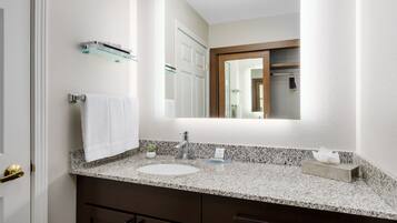 Une salle de bain avec un comptoir en granit, un lavabo blanc, un miroir et un porte-serviettes.