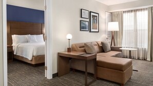 Une chambre d’hôtel avec un lit, un canapé, une petite table, une lampe et une fenêtre avec des rideaux.