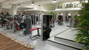 Un gimnasio con diferentes máquinas de ejercicio, piso de madera y una escalera.