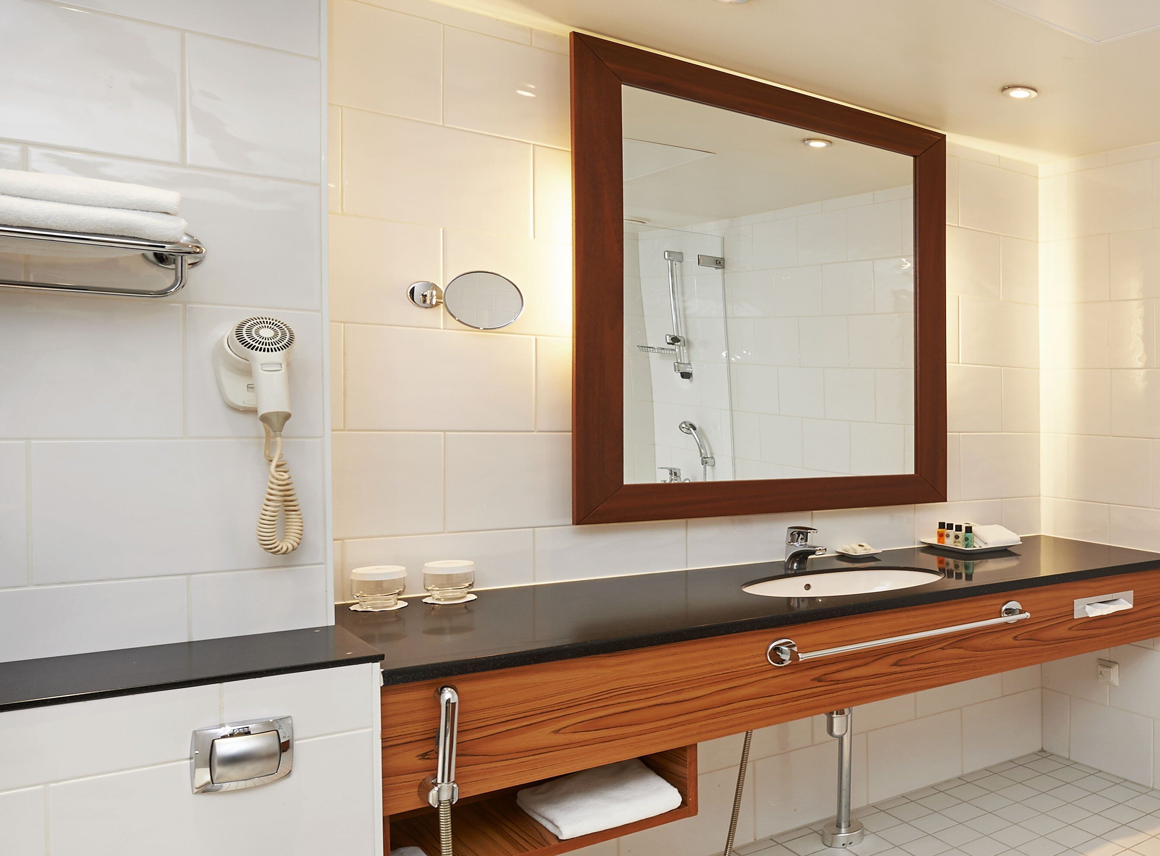 Un baño moderno con tocador de madera, un espejo, un secador de pelo y un perchero para toallas.