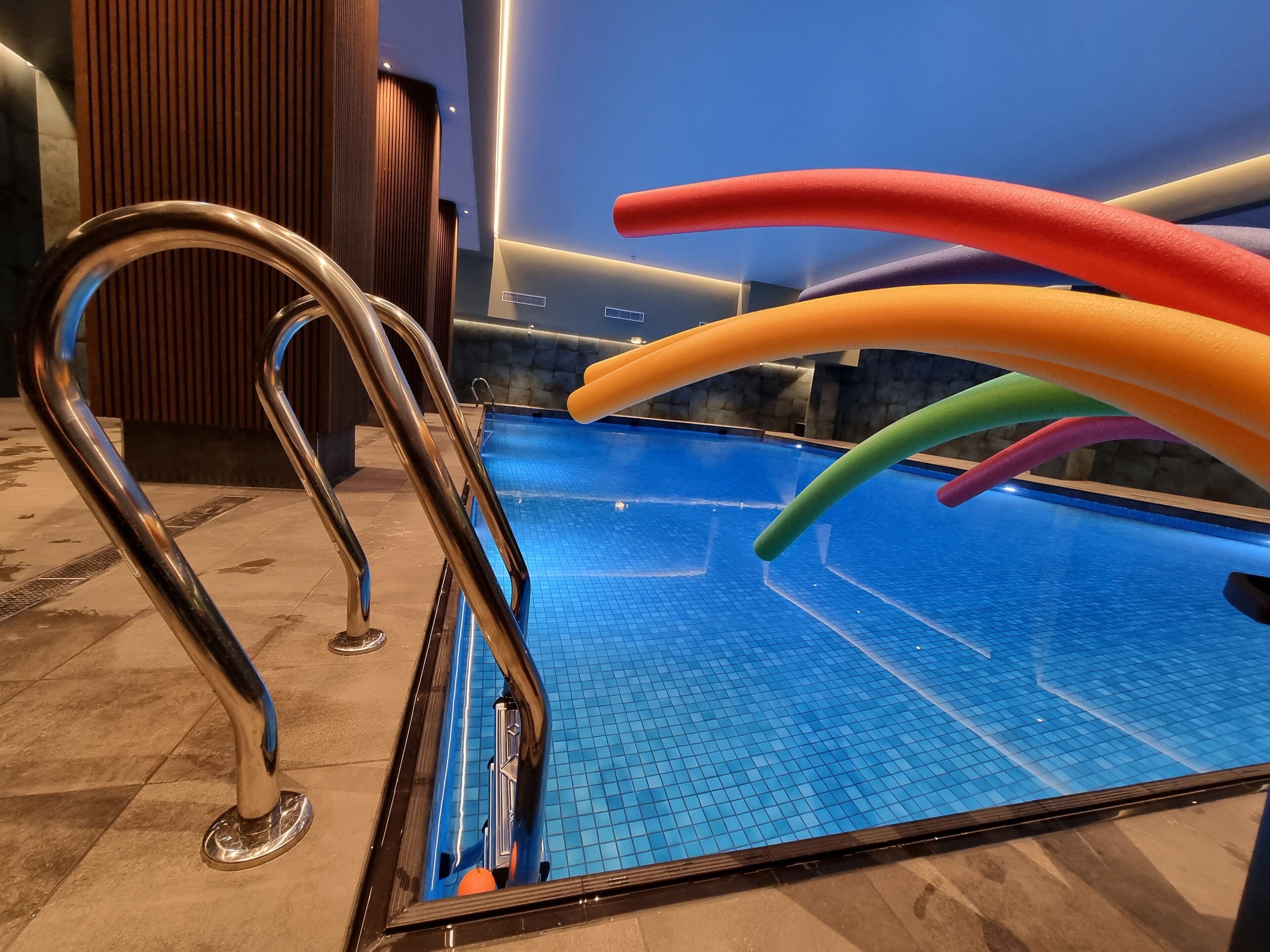 A swimming pool with a metal ladder and colorful floating tubes.