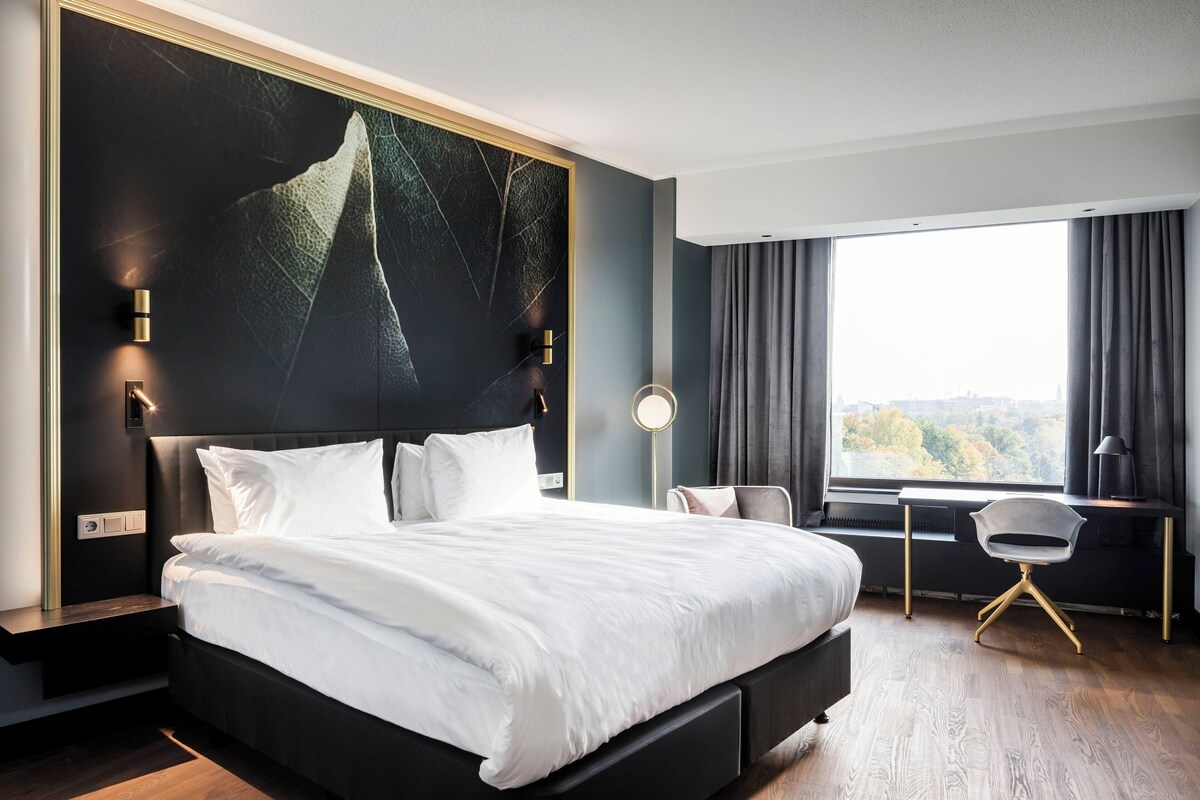A modern hotel room with a large bed, a desk, and a view of the city.