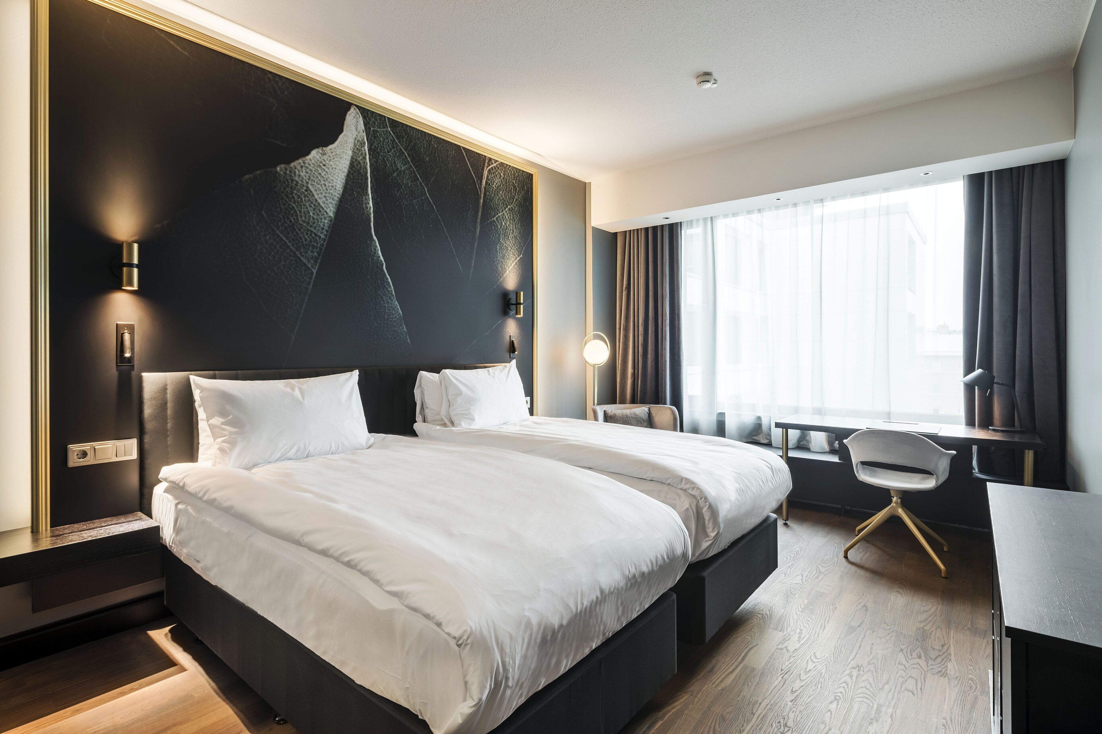 A modern hotel room with a large bed, a desk, and a chair.