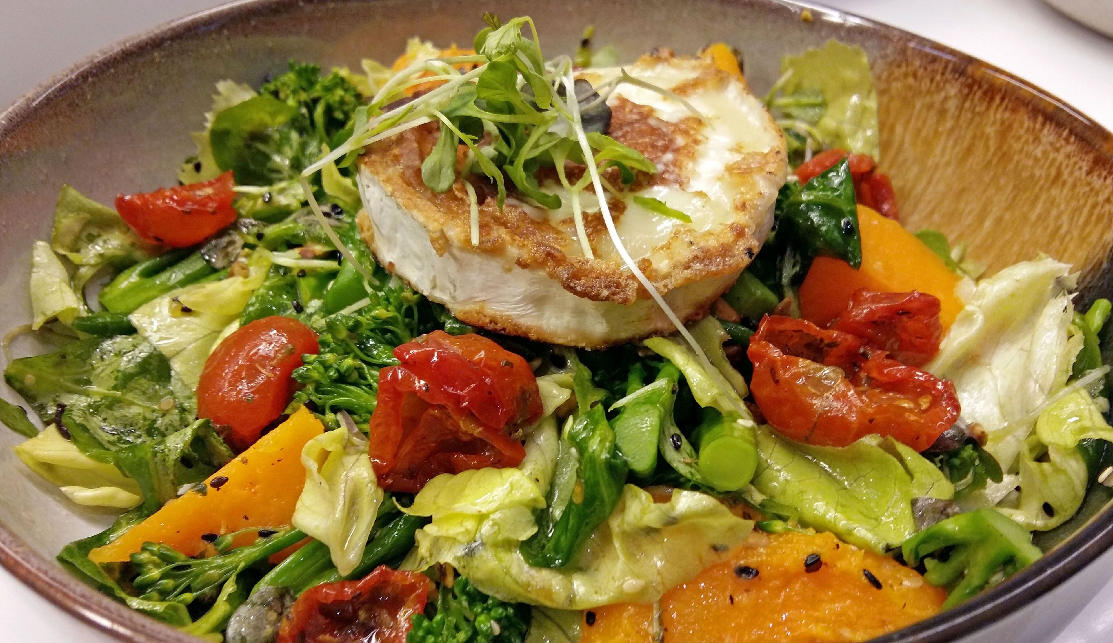 Ein Salat mit verschiedenen Gemüsesorten und einem Stück gegrilltem Hähnchen darauf.