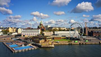 A waterfront cityscape with a prominent Ferris wheel, a historic church, and a swimming pool area.