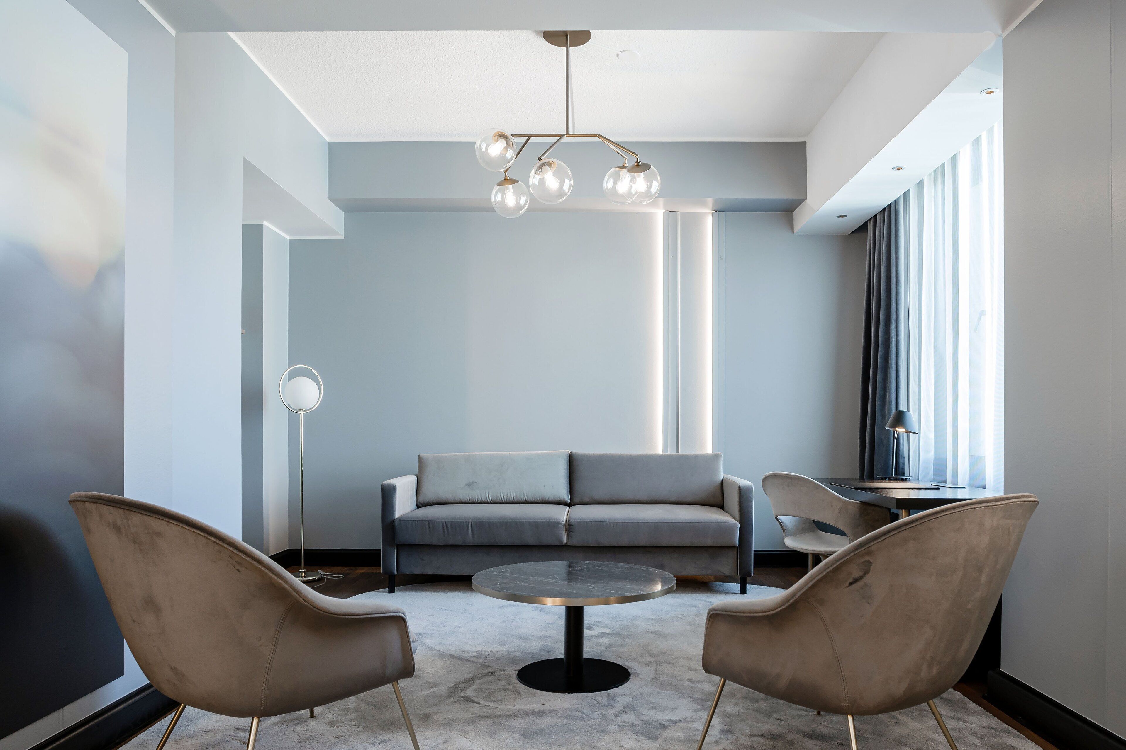 A modern living room with a grey sofa, two armchairs, a coffee table, and a chandelier.