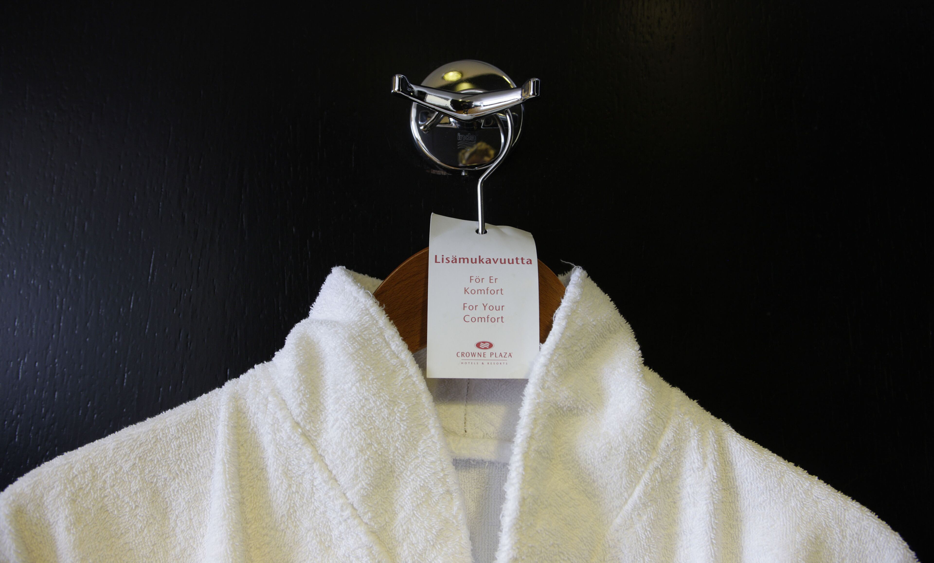 Un asciugamano bianco appeso a un gancio in metallo con un'etichetta che recita "Lisamukavuutta För Er Komfort For Your Comfort Crowne Plaza Hotels & Resorts".