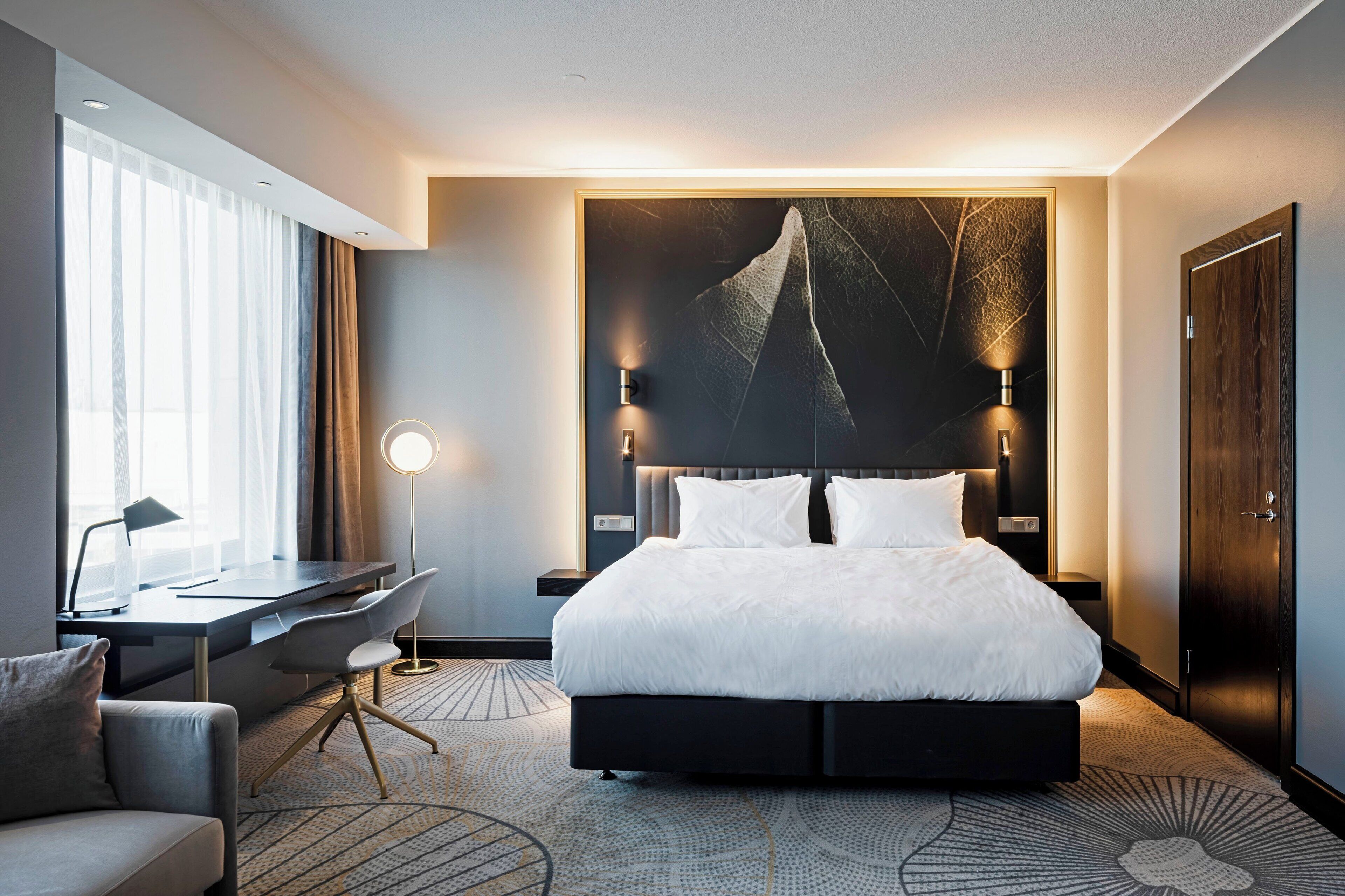 A modern hotel room with a large bed, a desk, and a chair.