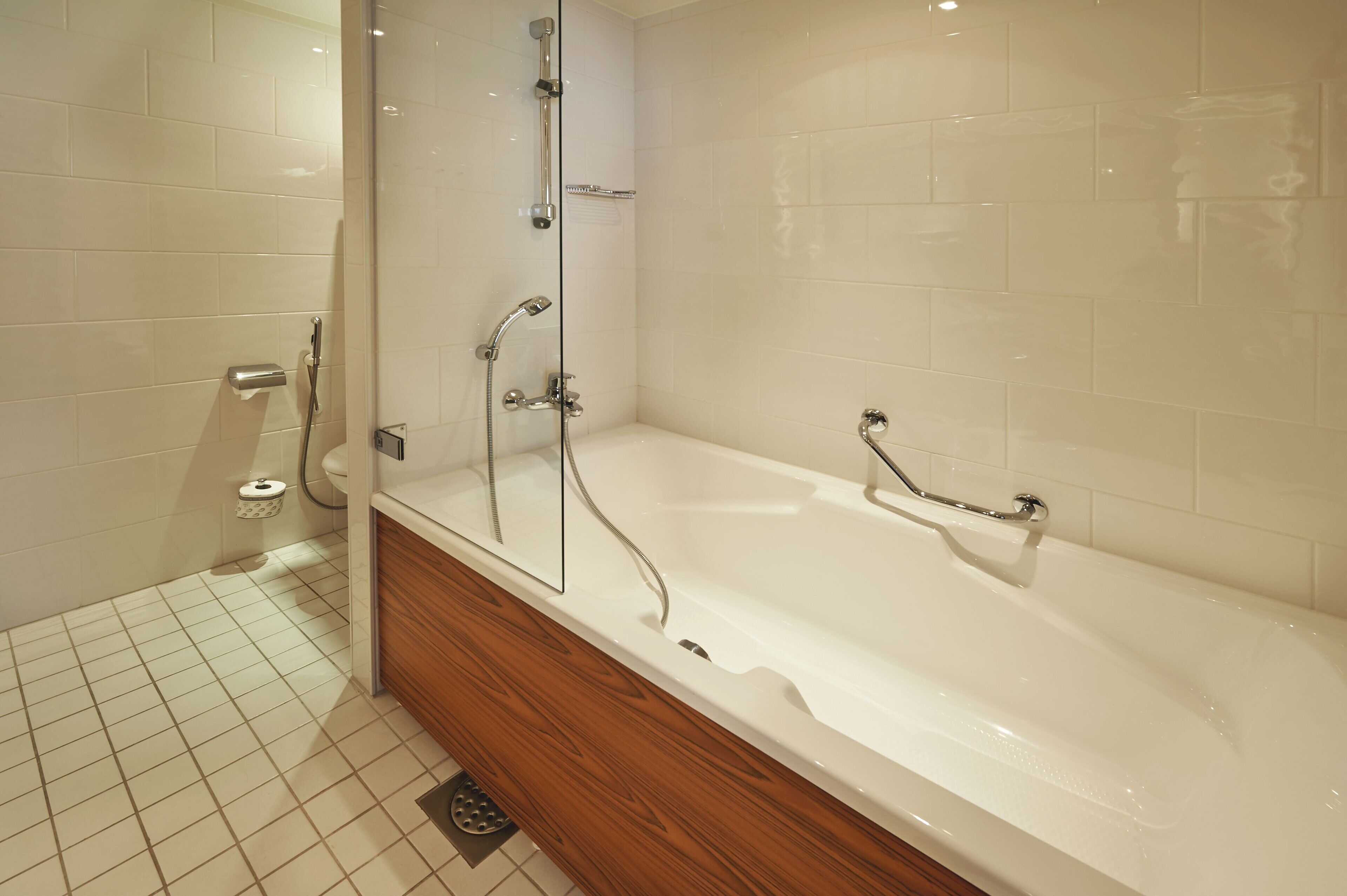 A modern bathroom with a white bathtub, wooden vanity, and a glass shower enclosure.