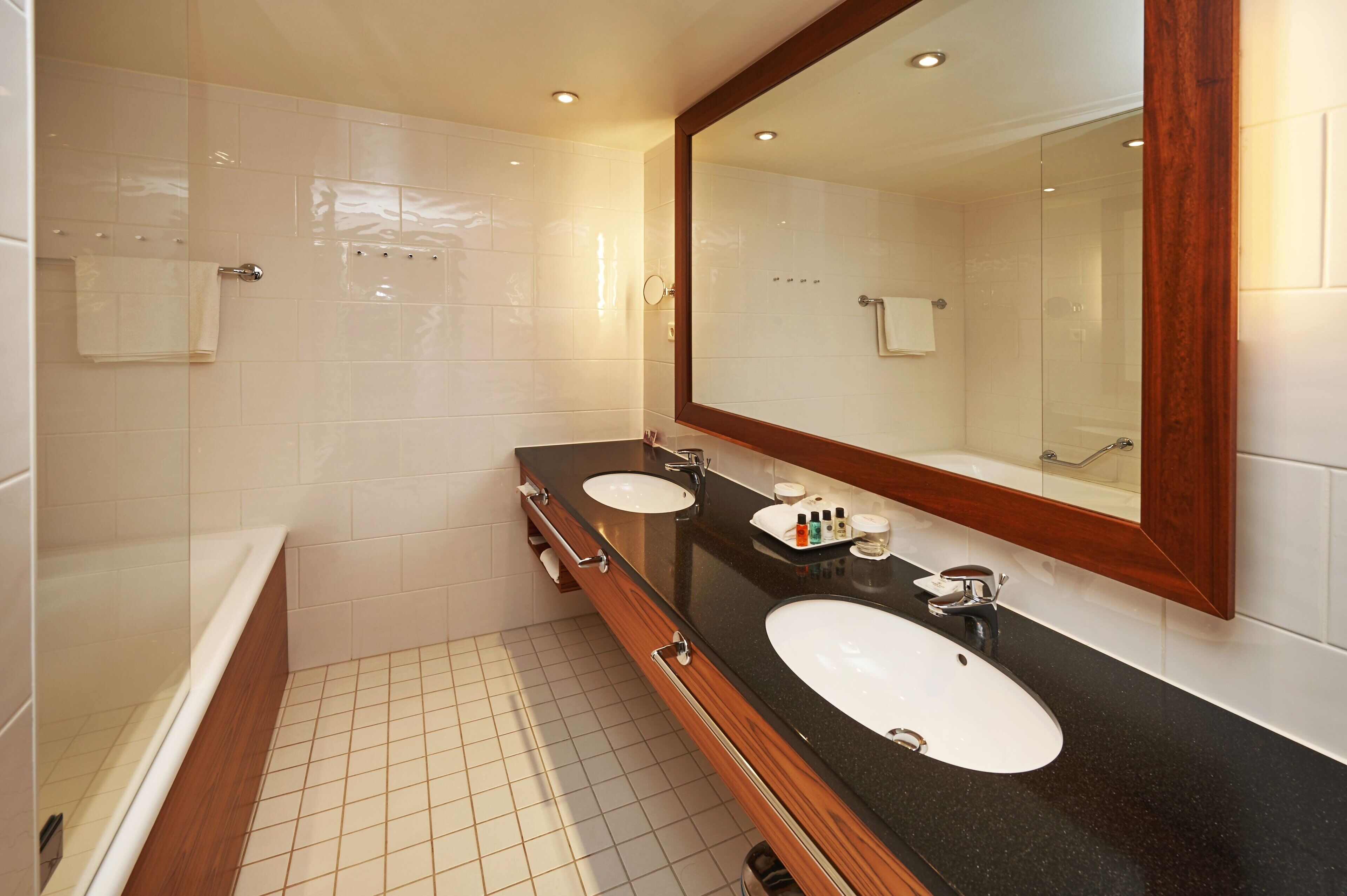 A modern bathroom with two sinks, a large mirror, and a bathtub.