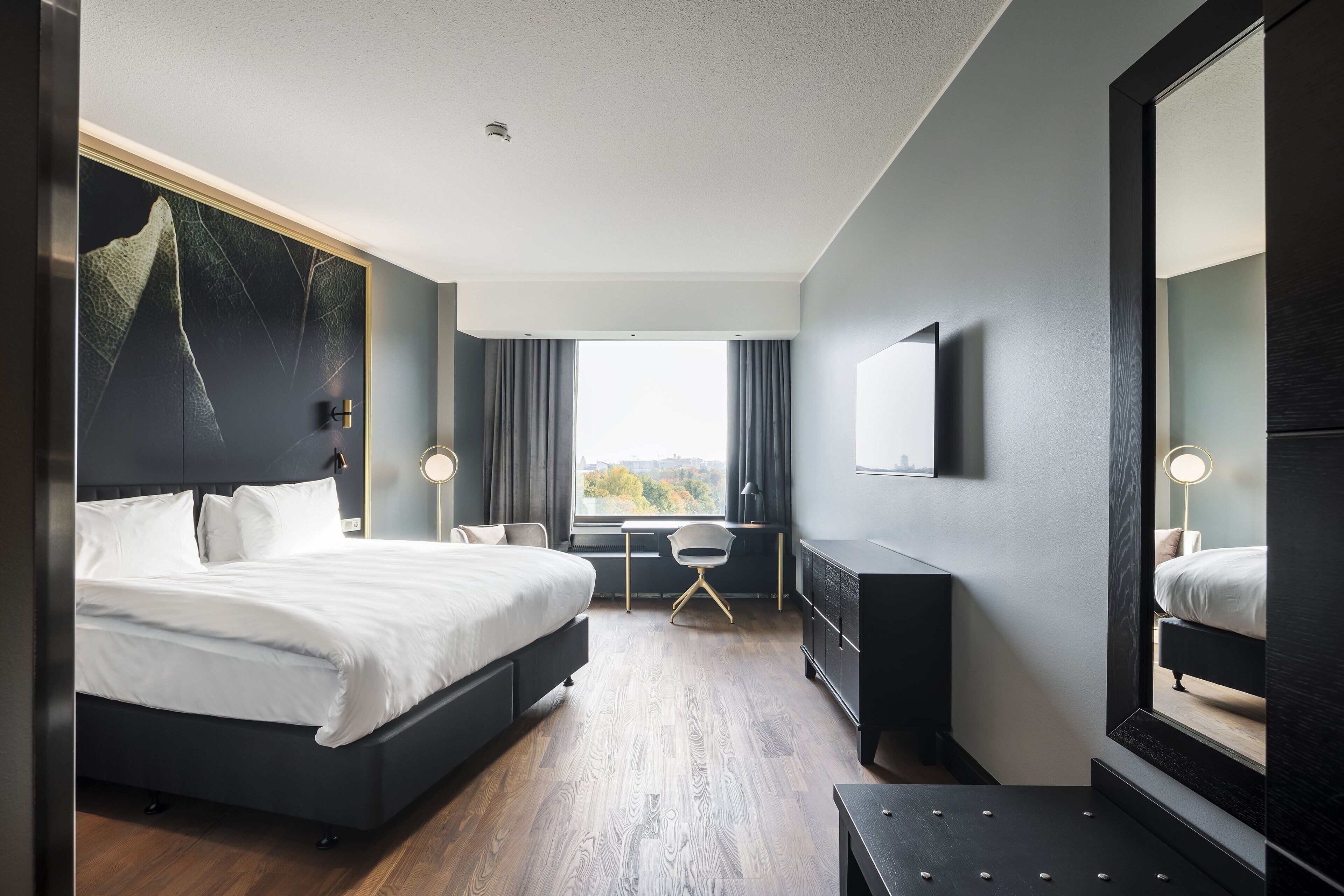 Et moderne hotelværelse med en stor seng, et skrivebord, en stol og udsigt til det fri.