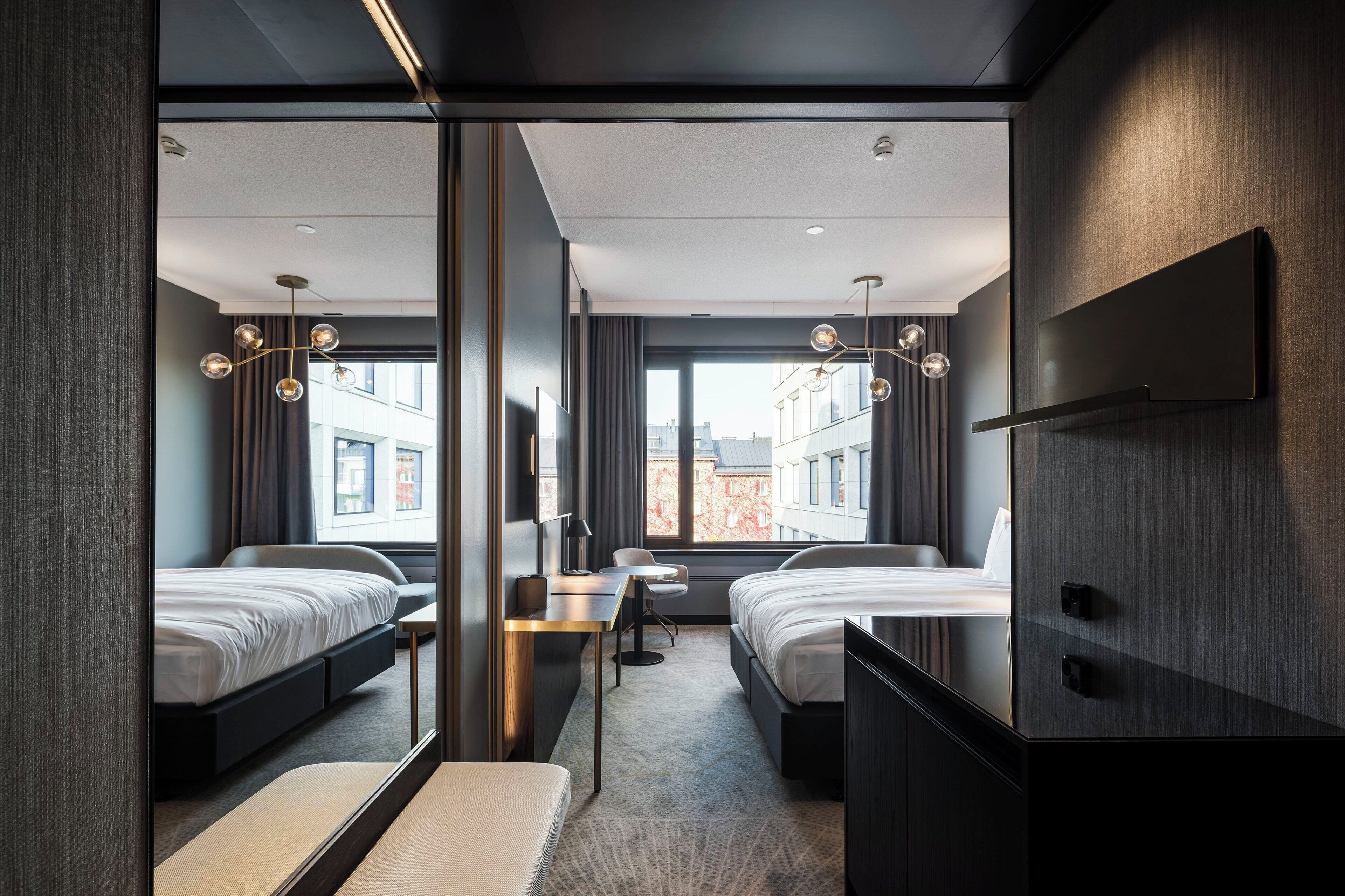 Habitación de hotel moderna con dos camas, un escritorio y un ventanal amplio con vistas a la ciudad.