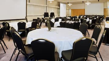 Un salón de conferencias con mesas redondas, sillas negras y una pantalla de proyector.
