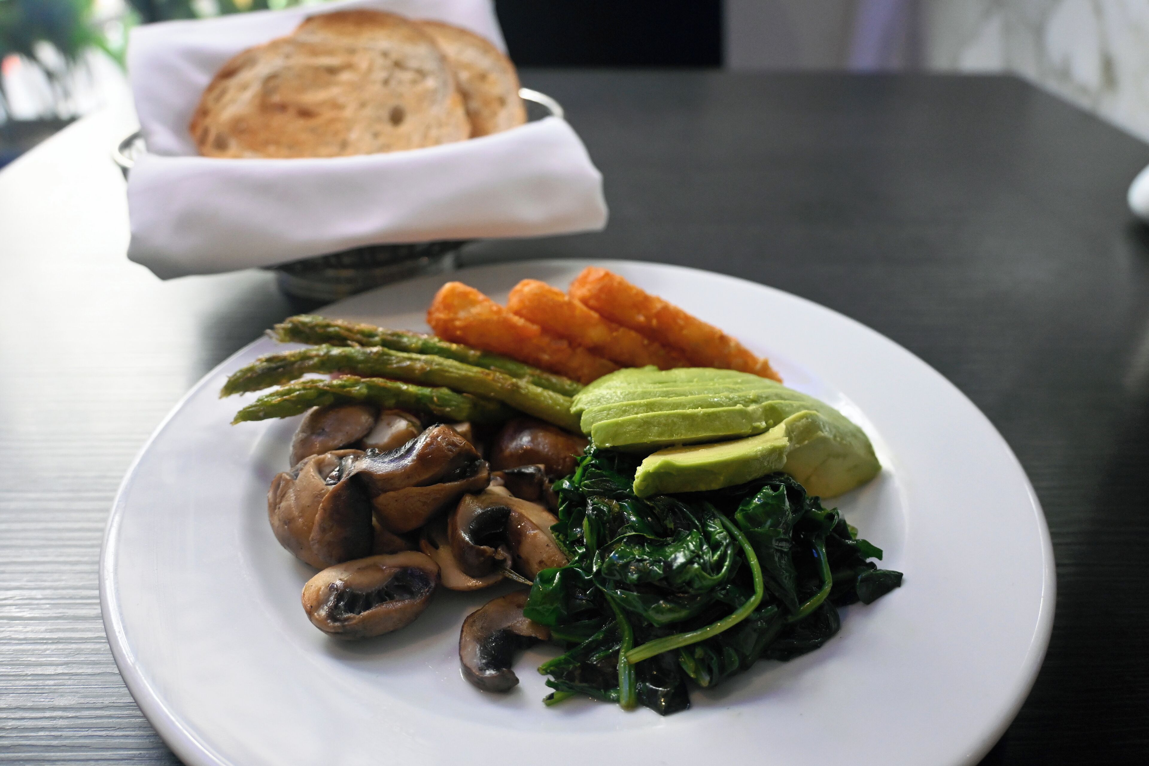 A plate of food with mushrooms, asparagus, spinach, and avocado on a white plate.
