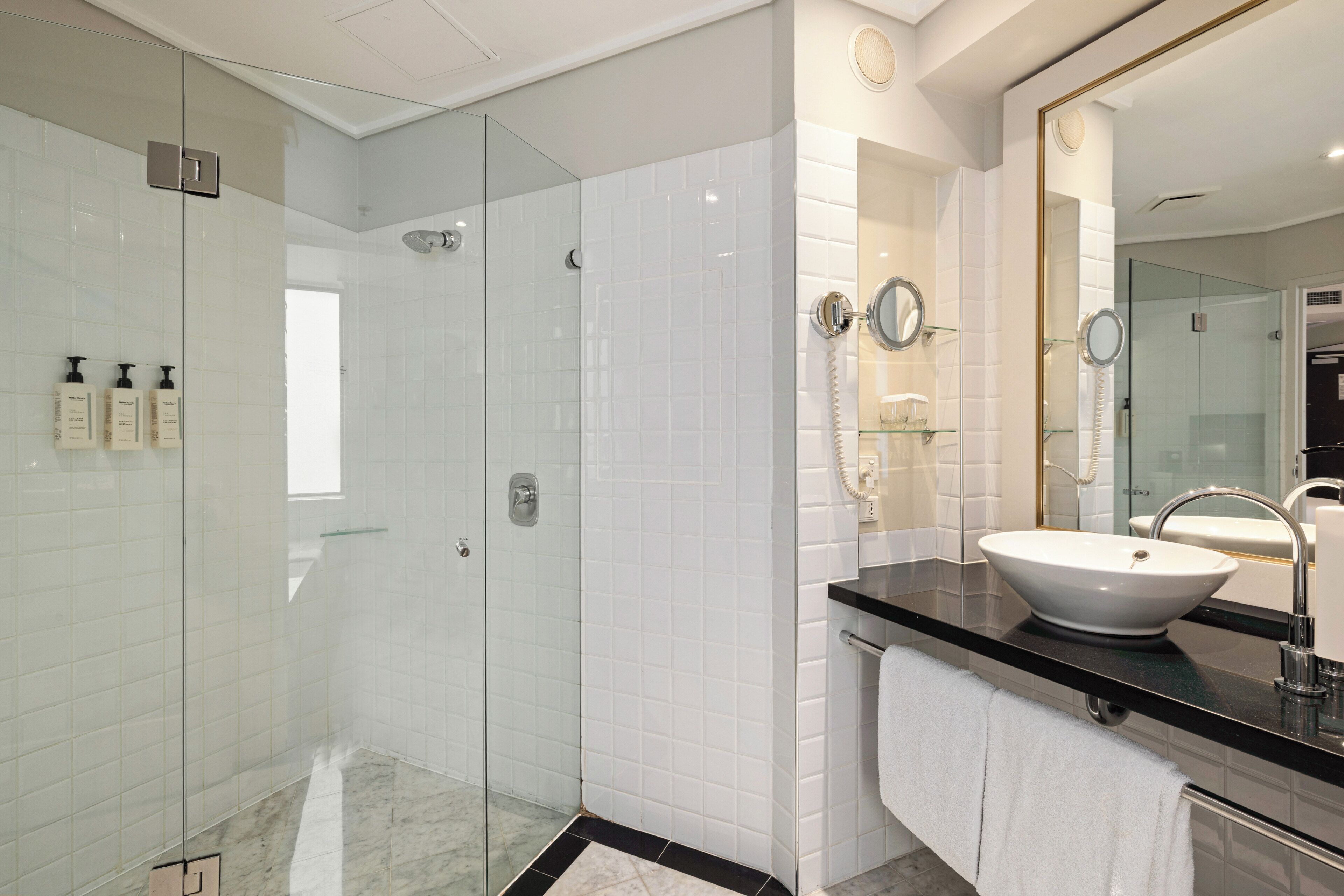 A modern bathroom with a glass-enclosed shower, a large mirror, and a white sink.