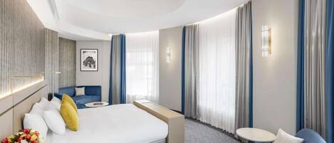 A modern hotel room with a large bed, a seating area, and a small table.
