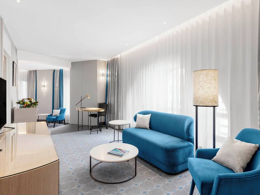 A modern hotel room with a flat-screen TV, a sofa, a coffee table, and a lamp.