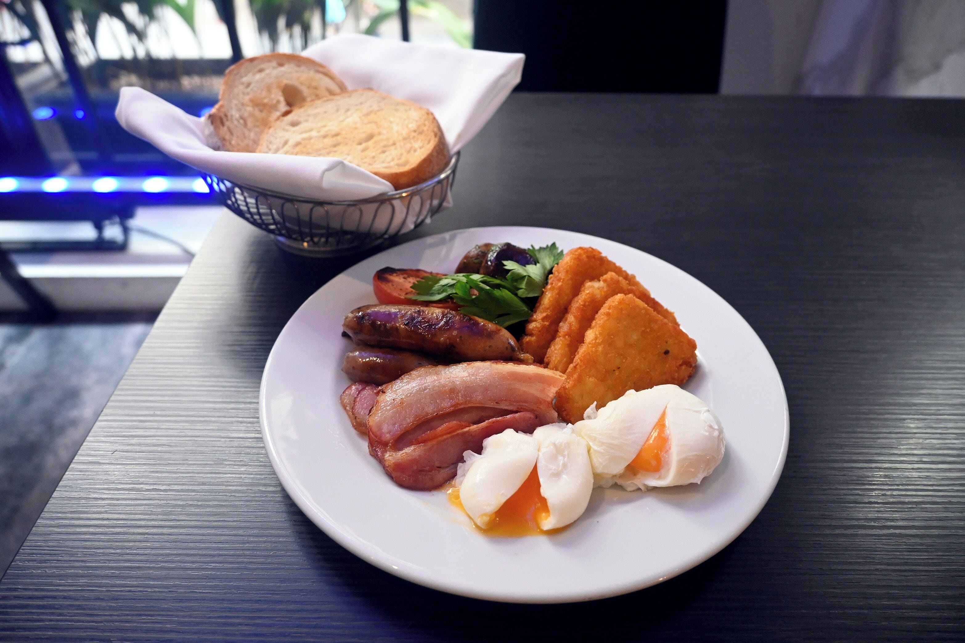 A plate of breakfast food including eggs, bacon, sausages, and toast on a table.