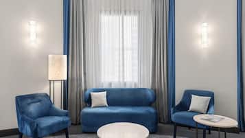 Una habitación moderna con un sofá azul, dos sillones, una mesa redonda y una lámpara de pie.