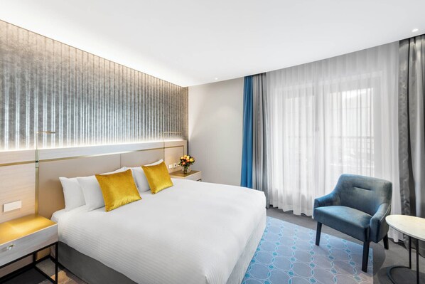 Una habitación de hotel con una cama grande, una mesita de noche, una silla y una pequeña mesa.