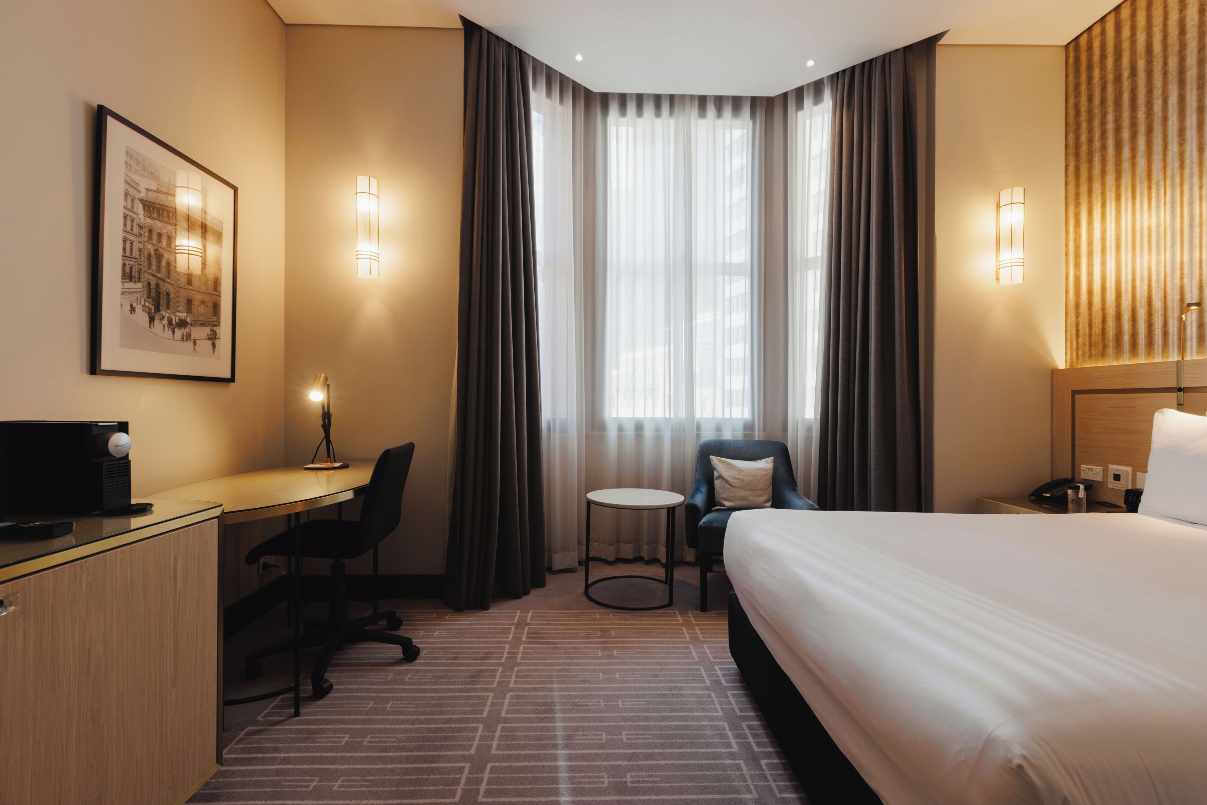 A hotel room with a bed, desk, chair, and a small table.