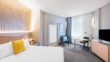 A hotel room with a bed, desk, chair, TV, and a large window with curtains.