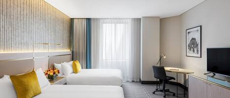 A hotel room with two beds, a desk, a chair, a television, and a window with curtains.