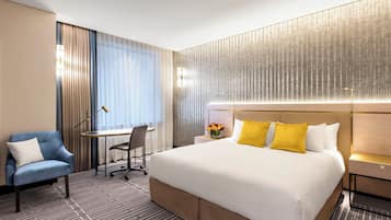 Quarto de hotel com uma cama grande, uma escrivaninha, uma cadeira e uma mesa de cabeceira com abajur.