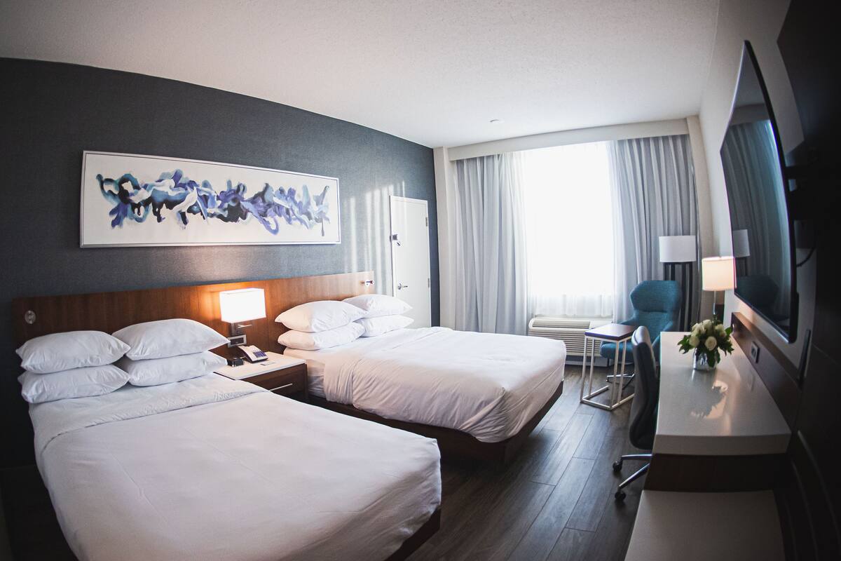 Une chambre d’hôtel avec deux lits, un bureau, une chaise, une télévision et un tableau au mur.